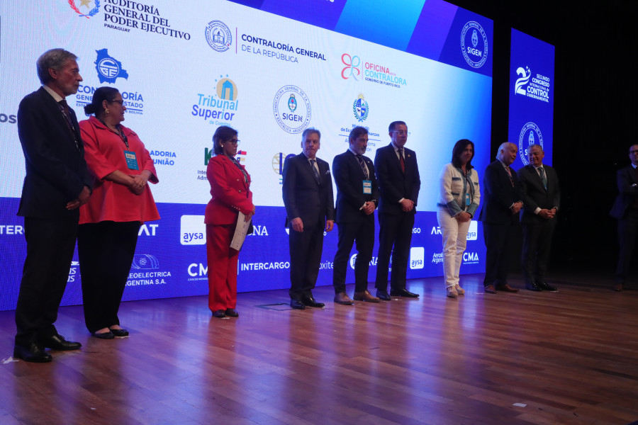 Nove oradores de pé no palco com o cartaz do congresso projetado ao fundo