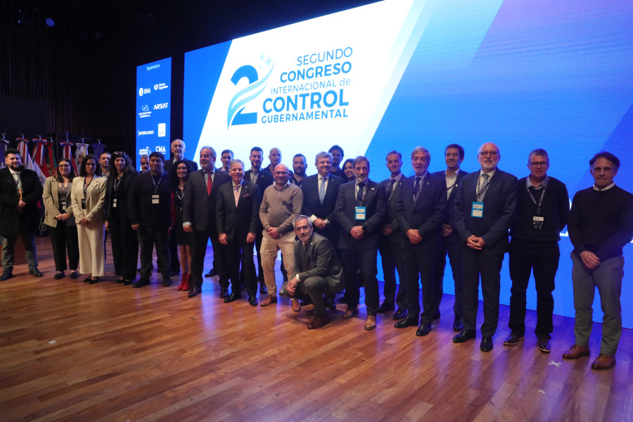 Foto de grupo de vários participantes de pé no palco em frente ao cartaz do congresso
