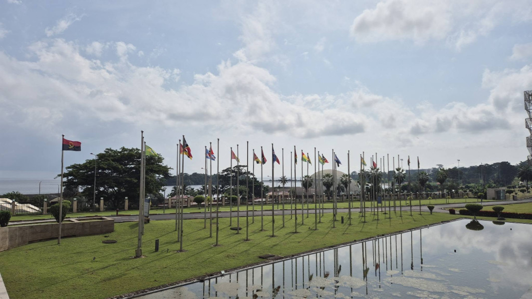 Área exterior com uma fileira de bandeiras de vários países dispostas ao longo de um relvado e um espelho de água