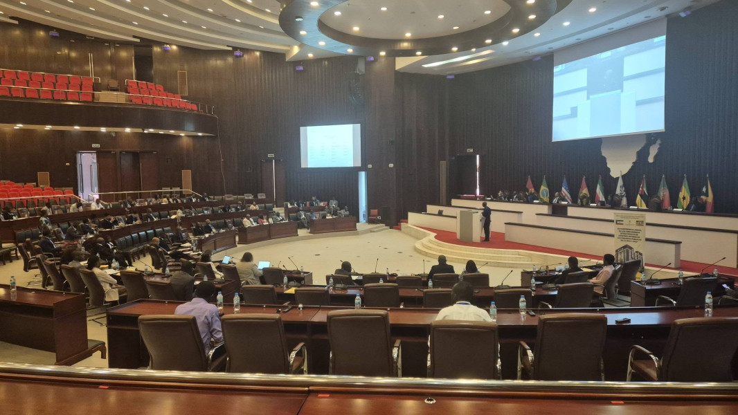 Auditório preenchido com participantes sentados em mesas curvas e com uma apresentação no fundo da sala