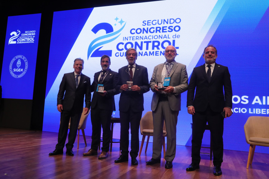 Cinco oradores de pé no palco com o cartaz do congresso projetado ao fundo
