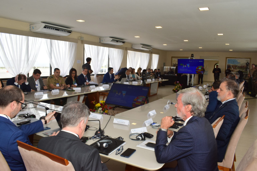 Vista panorâmica da mesa de reunião numa sala com vários participantes sentados