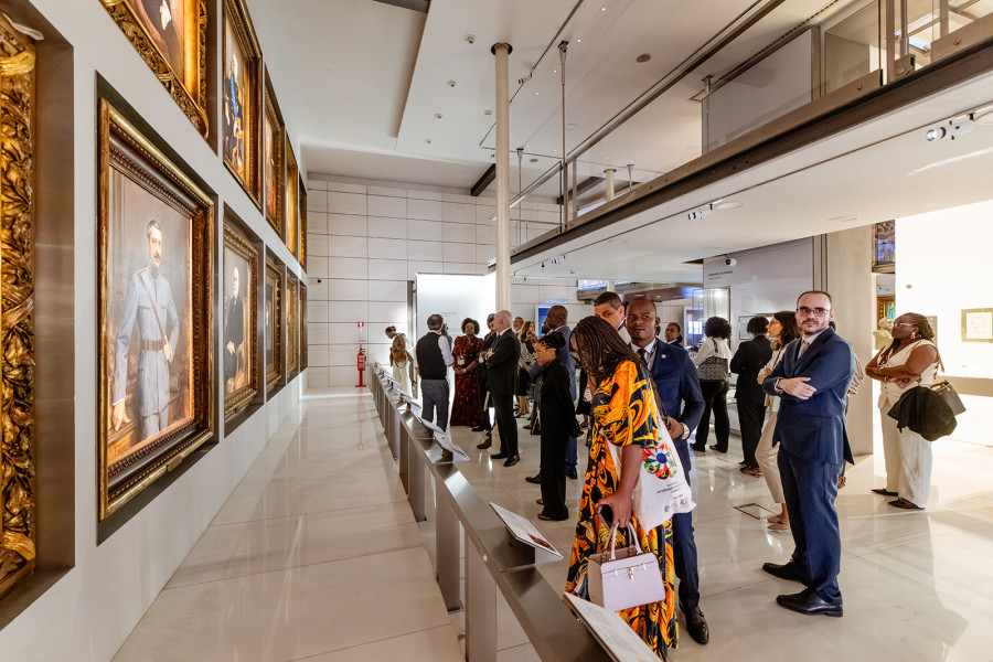 Várias pessoas durante uma visita a uma exposição numa galeria onde se encontram expostos alguns quadros.