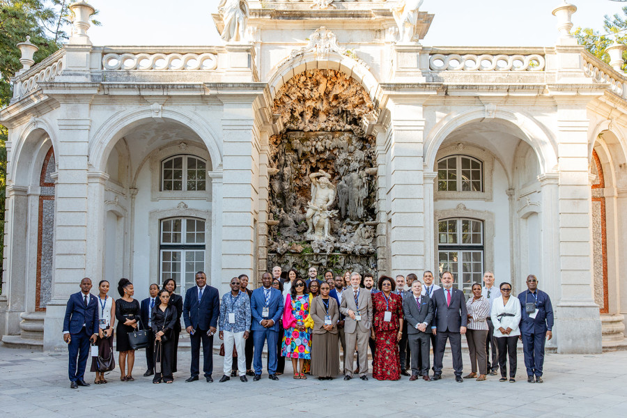 Grupo de participantes da conferência reunido no exterior, em frente a uma imponente estrutura arquitetónica com uma cascata e escultura.