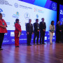 Nove oradores de pé no palco com o cartaz do congresso projetado ao fundo