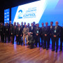 Foto de grupo de vários participantes de pé no palco em frente ao cartaz do congresso