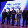 Cinco oradores de pé no palco com o cartaz do congresso projetado ao fundo