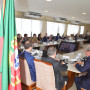 Vista da mesa de reunião numa sala com vários participantes sentados com a bandeira portuguesa em primeiro plano