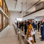 Várias pessoas durante uma visita a uma exposição numa galeria onde se encontram expostos alguns quadros.