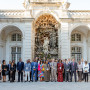 Grupo de participantes da conferência reunido no exterior, em frente a uma imponente estrutura arquitetónica com uma cascata e escultura.
