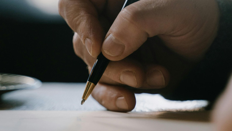 Pormenor de uma mão a segurar uma caneta, a escrever num papel com fundo desfocado